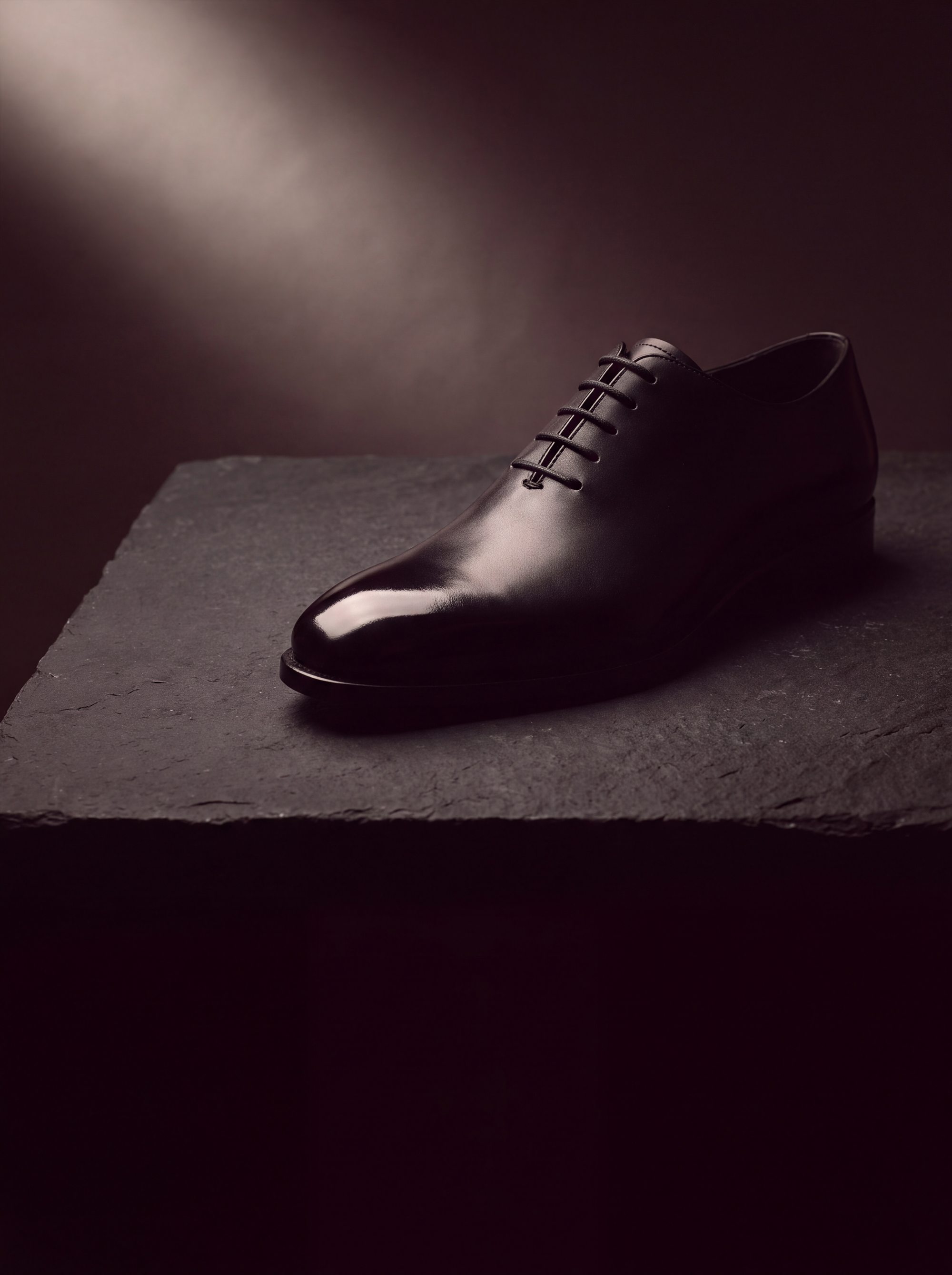 A black wholecut oxford on a slate slab, lit from one side.